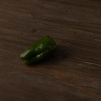 木目調のフローリングに落ちた緑色のピーマンの写真