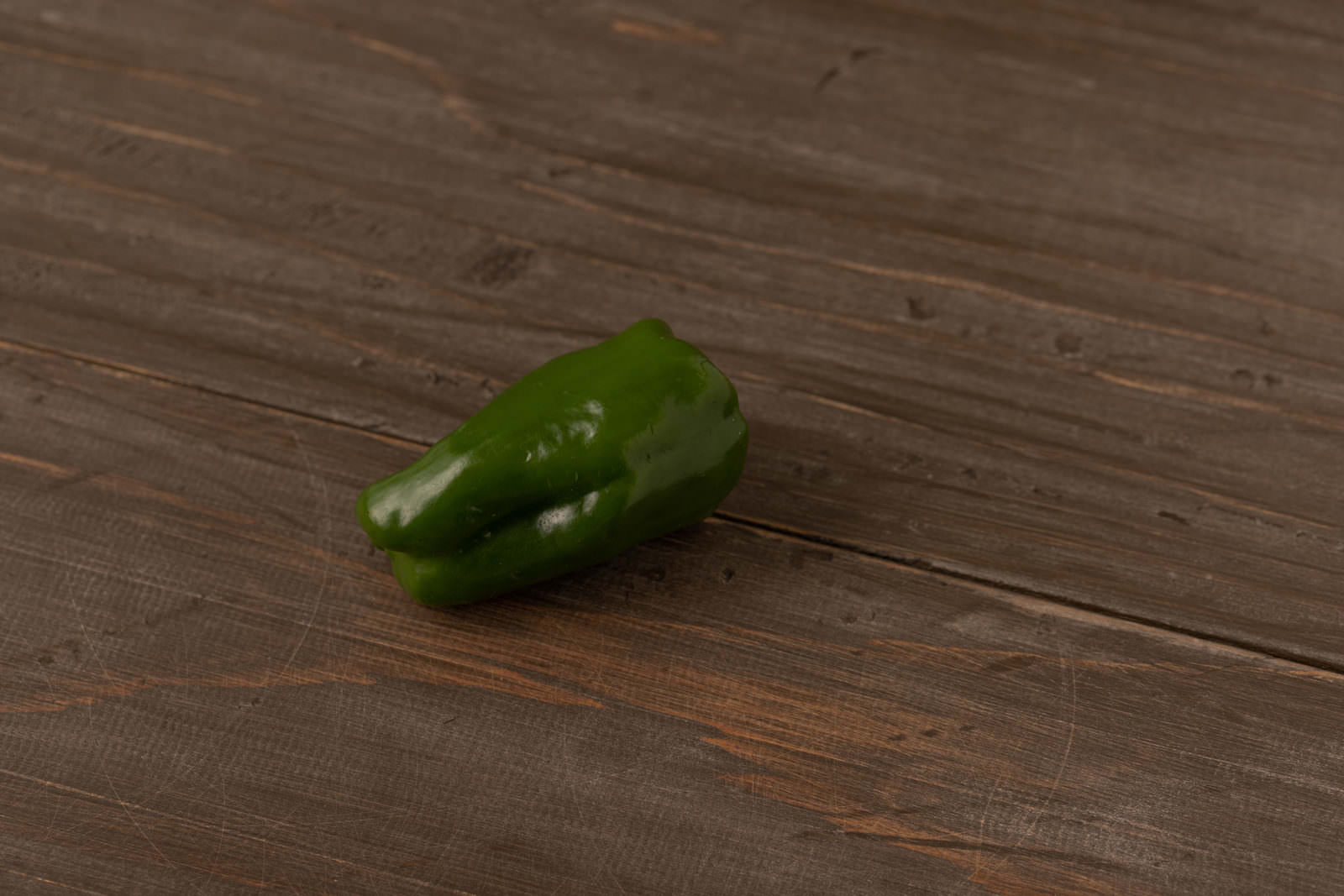 木目のフローリングの上に置かれた緑色のピーマン1個