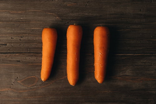 木製テーブルに並んだオレンジ色のニンジン3本の食材
