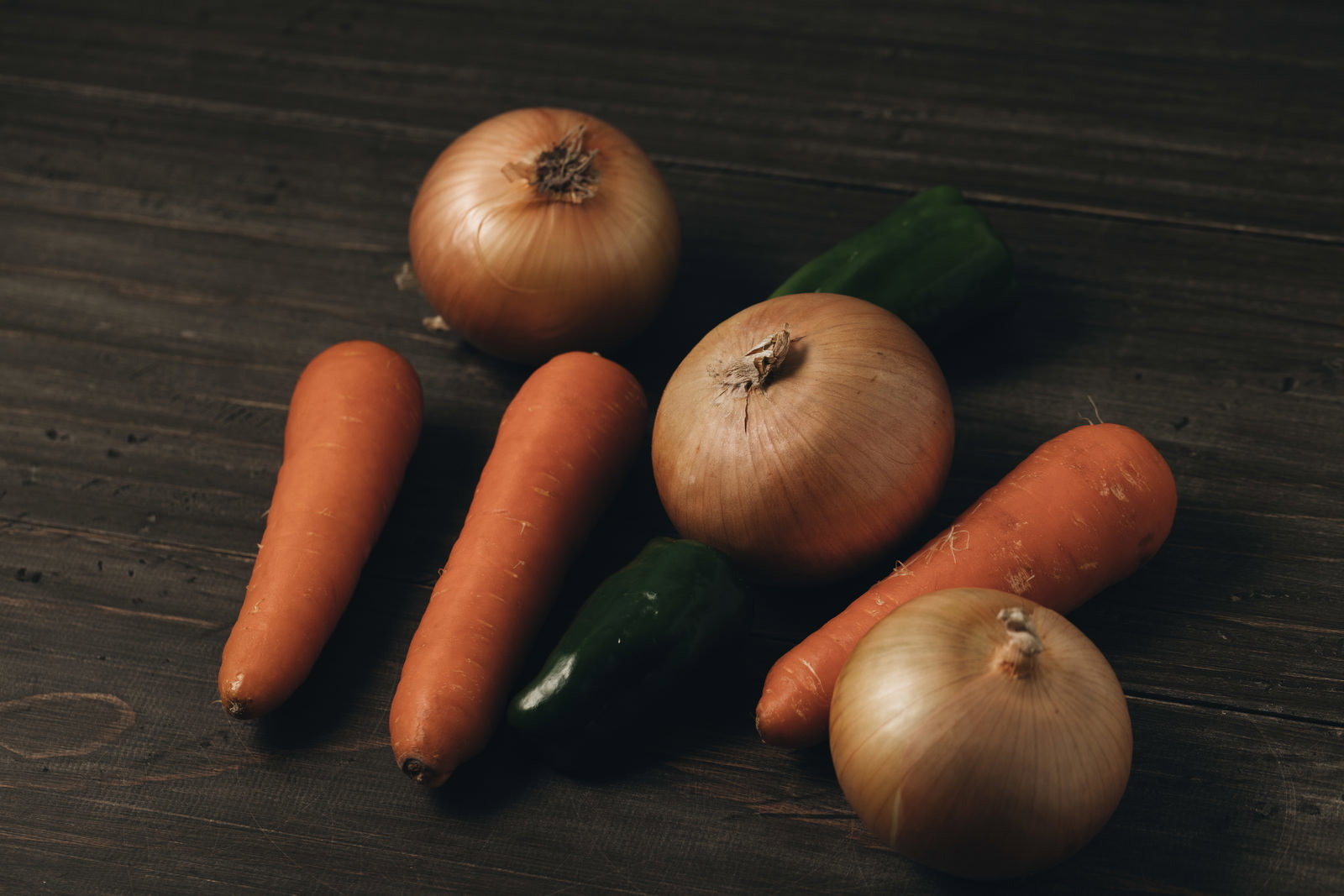 暗い木製のテーブルの上に置かれた玉葱、人参、ピーマンの食材写真