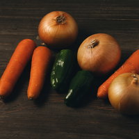 取り寄せた野菜の人参、玉葱、ピーマンを木製テーブルに並べた様子の写真