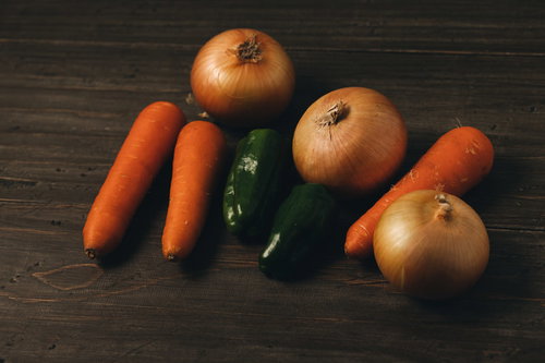 取り寄せた野菜の人参、玉葱、ピーマンを木製テーブルに並べた様子