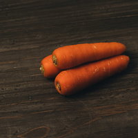 木目調の表面に重なって置かれた三本のニンジンの写真