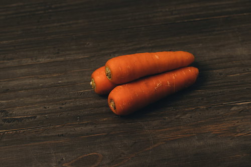 木目調の表面に重なって置かれた三本のニンジン