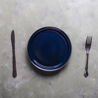 濃紺のお皿のサイドに置かれたフォークとナイフの写真