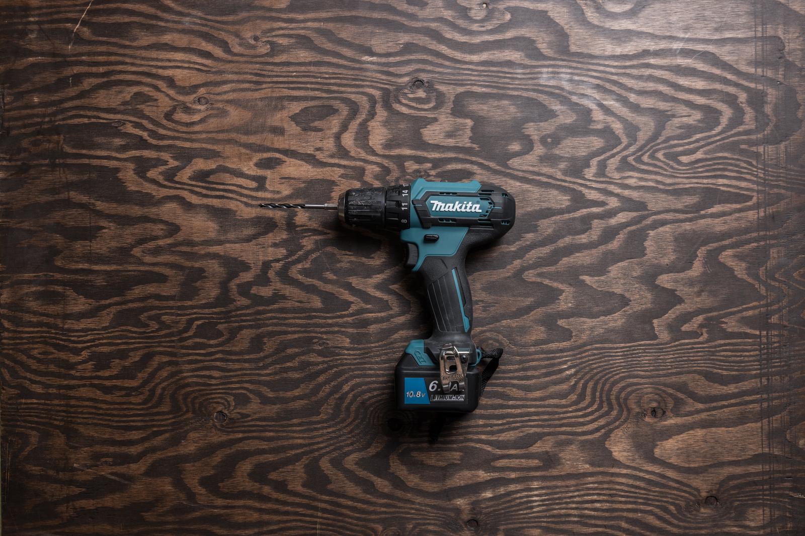 木目板の上に置かれた青いマキタ製のドライバドリルと黒いバッテリー