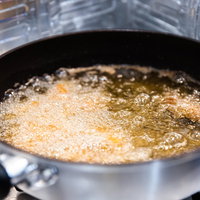 フライパンで加熱する調理中の天ぷら油と食材の揚げ物調理の写真