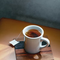 窓辺に置かれた白いティーカップの紅茶と木製コースターの写真