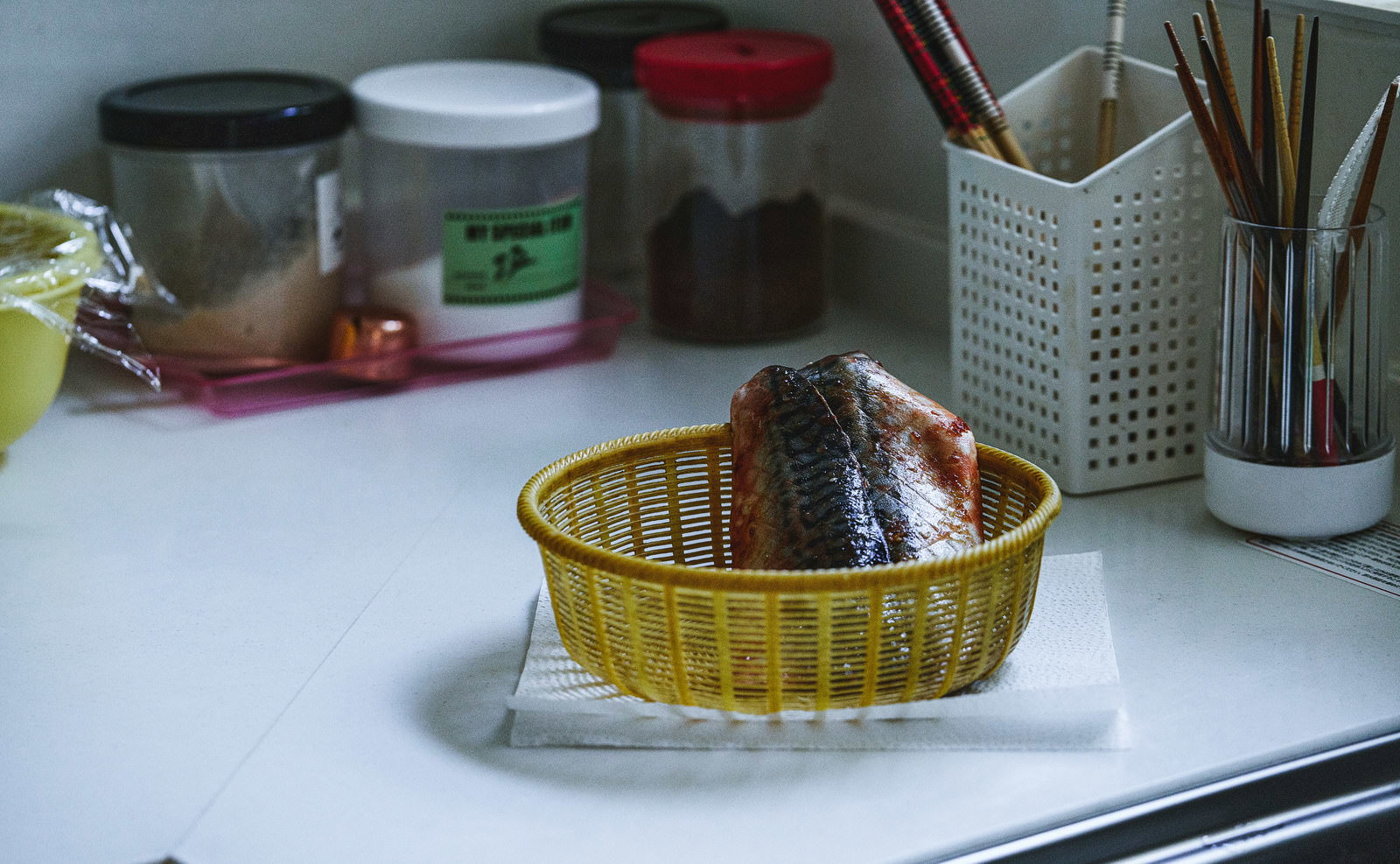 黄色いざるに入った鯖が薄暗いキッチンのカウンターに置かれている