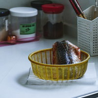 薄暗いキッチンに置かれた黄色いザルに入った新鮮な鯖の写真