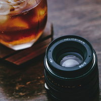 冷たい麦茶とカメラレンズが置かれた木製テーブルの写真