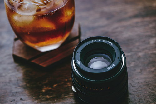 冷たい麦茶とカメラレンズが置かれた木製テーブル