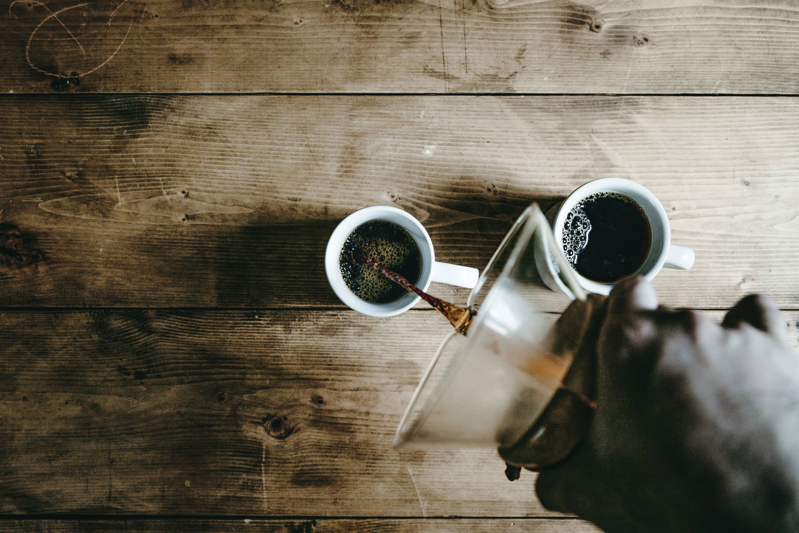 木目のテーブルでコーヒーメーカーから白いマグカップにコーヒーを注ぐ様子