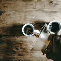 木目のテーブルでコーヒーメーカーから白いマグカップに注ぐ風景の写真