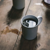 床にこぼれたホットコーヒーとマグカップ、木製テーブルの写真