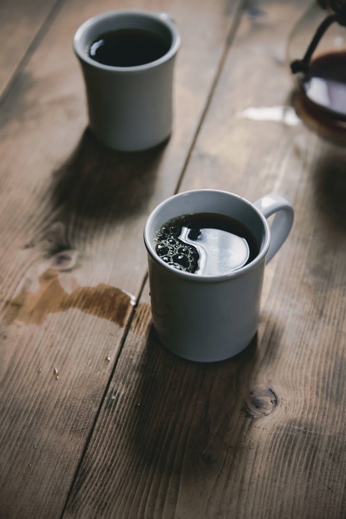 床にこぼれたホットコーヒーとマグカップ、木製テーブル