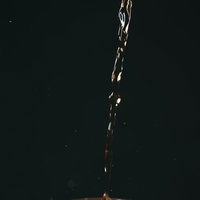 透明なグラスに勢いよく注ぐ琥珀色の麦茶のスプラッシュの写真