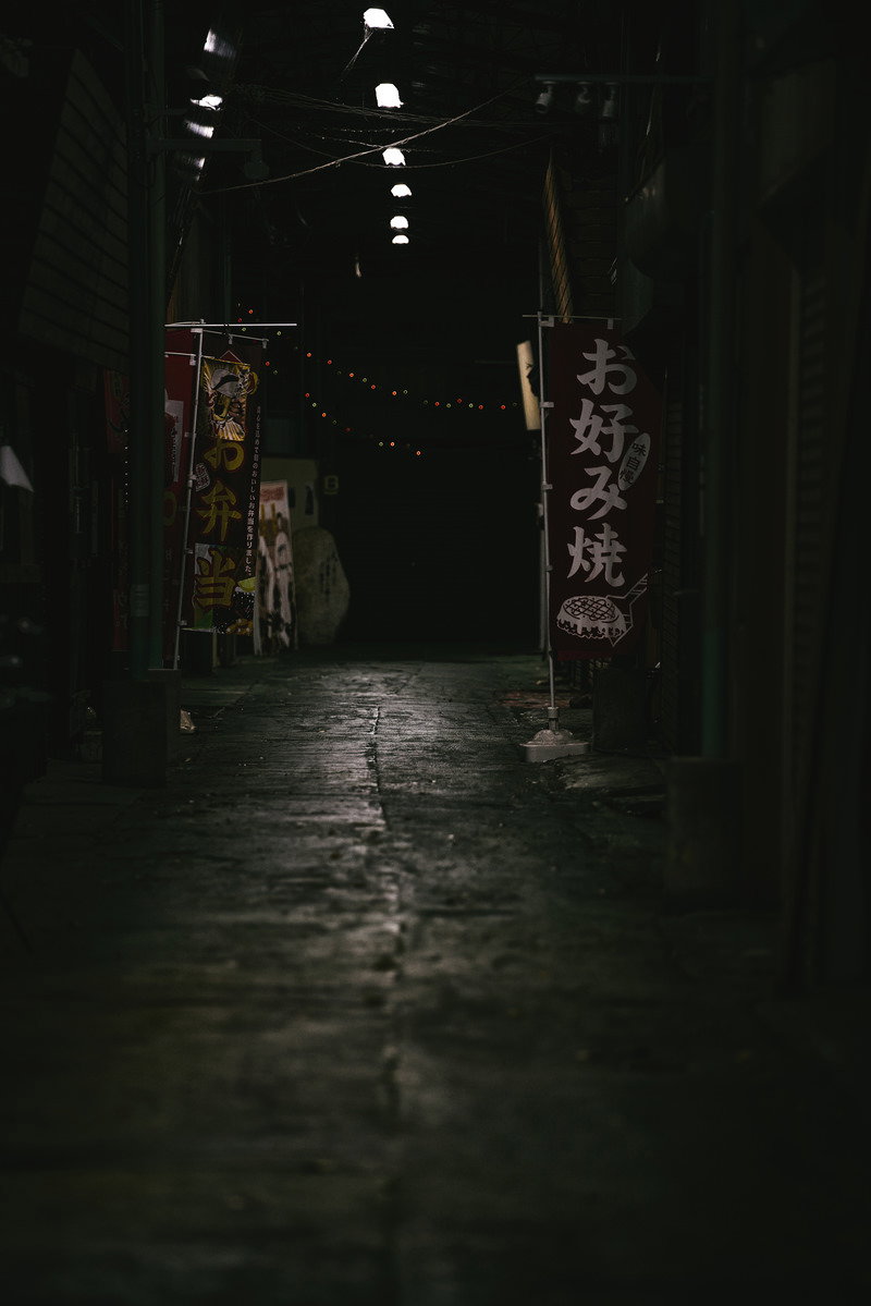 夜の薄暗い路地に旗が掲げられ、街灯の光が石畳を照らしている