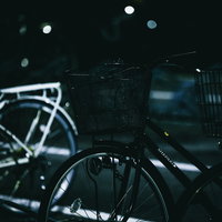 早朝の薄暗い駐輪場に並ぶ自転車と街灯の光の写真