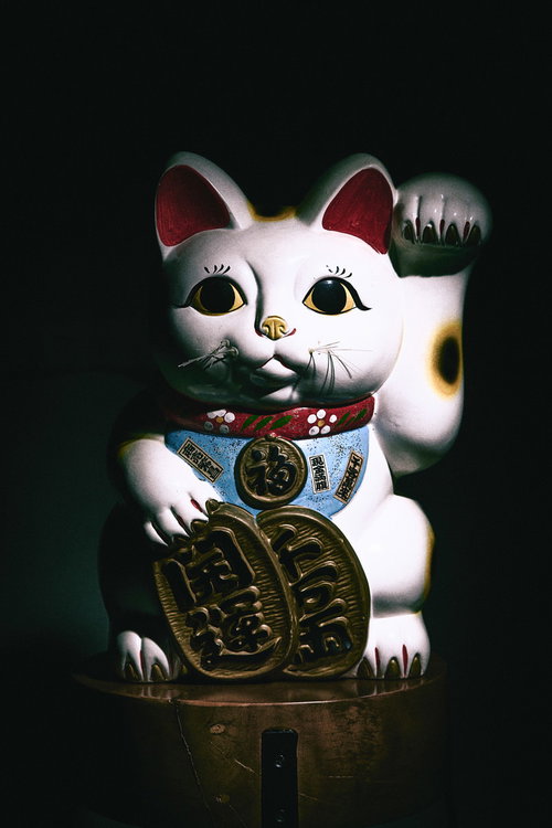 暗がりで右手を上げた金色装飾の招き猫の置物