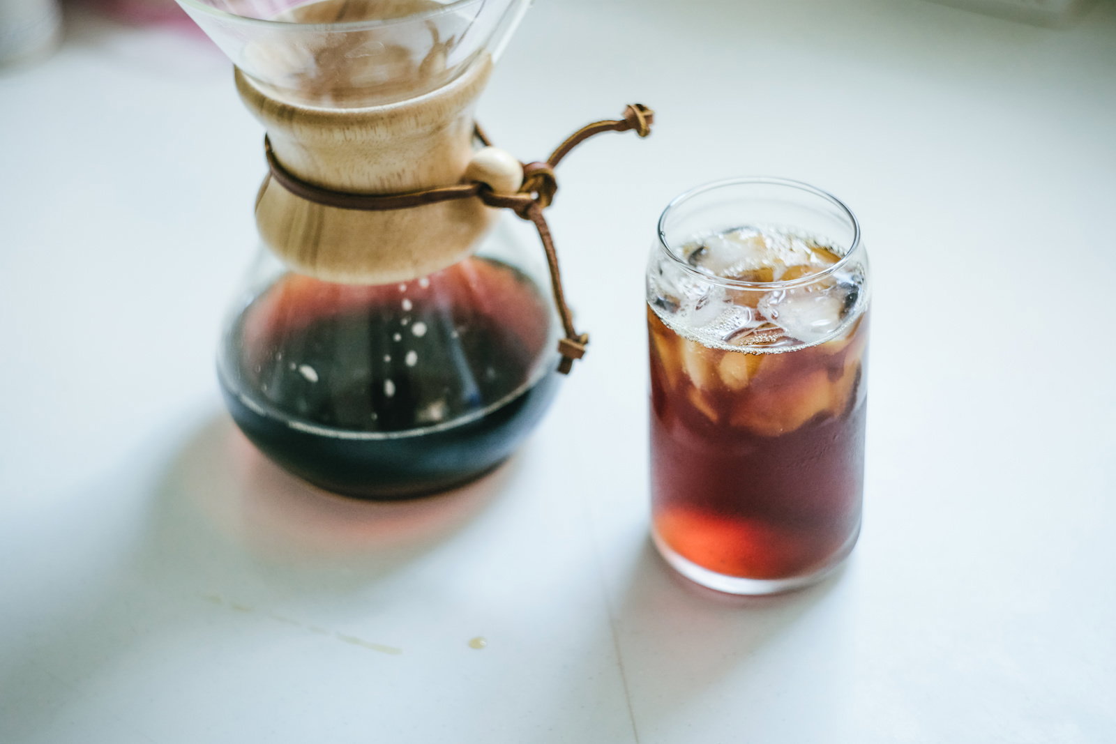 白いテーブルの上に置かれたガラス製コーヒーメーカーと氷入りアイスコーヒーのグラス