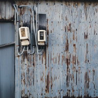 錆び付いた波板の外壁に取り付けられた電気メーターの写真