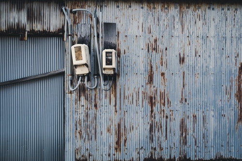 錆び付いた波板の外壁に取り付けられた電気メーター