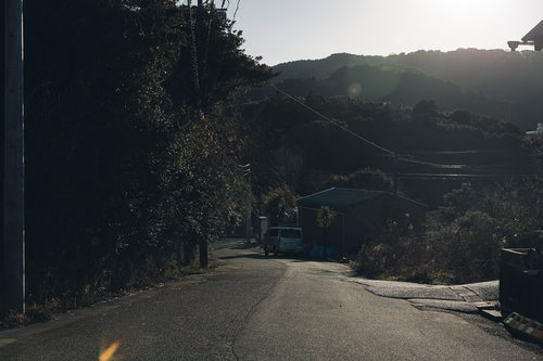 山林に囲まれた緑生い茂る下り坂に停まる白いバン