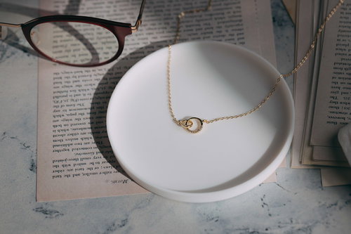 白い皿の上に置かれたゴールドネックレスと眼鏡