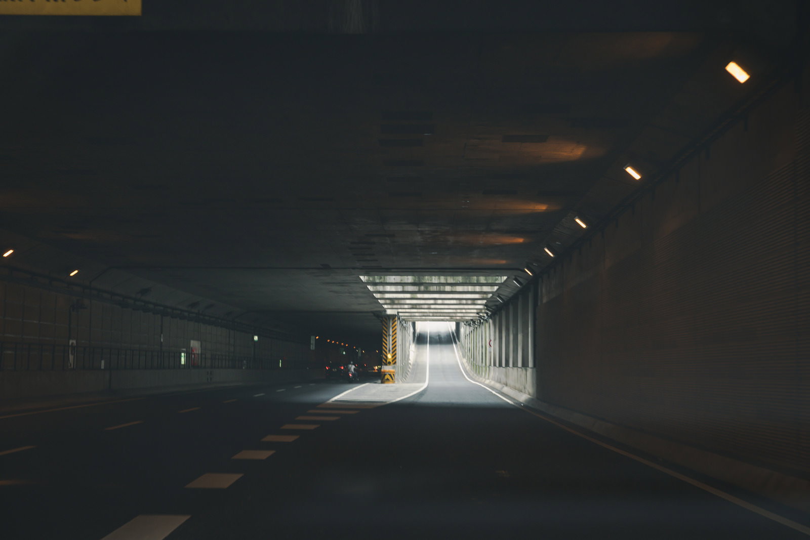 明るい出口に向かうアンダーパスの車線。照明が並び、前方から光が差し込んでいる