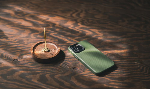 木目のテーブルに置かれた緑色のスマートフォンとお香立ての風景