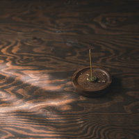 木目の机に置かれたお香立てから立ち上る煙の写真