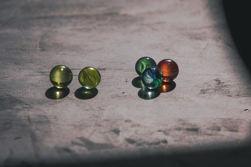 木の表面に転がるカラフルなビー玉と映る影