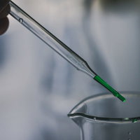 スポイトで採取する緑色の液体と試験管を使用した実験の写真