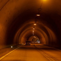 オレンジ色の照明が灯るトンネル内を走行中の自動車の写真