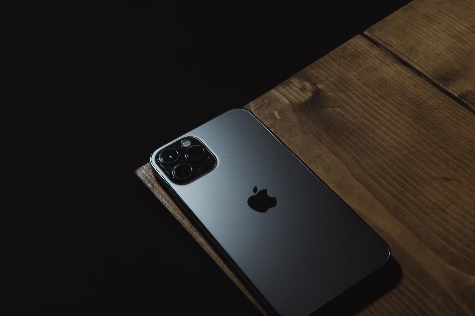 木目のテーブル端に置かれたケース未装着のシルバーiPhone