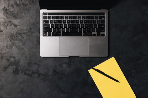 ノートパソコンと黄色いメモ帳を並べたデスク上の配置