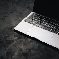 暗がりに置かれたシルバーのMacbookの光と影の写真