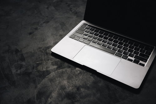 暗がりに置かれたシルバーのMacbookの光と影