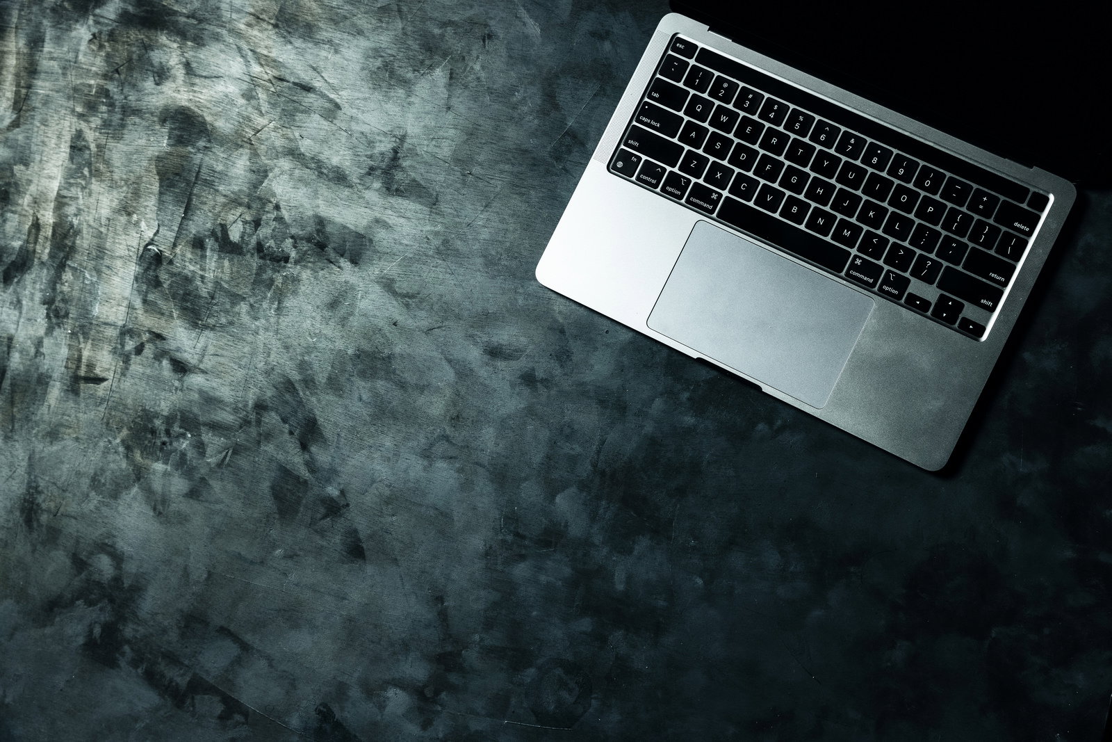 粗いコンクリート調のテーブルに置かれたシルバーのMacBookを上から見た写真