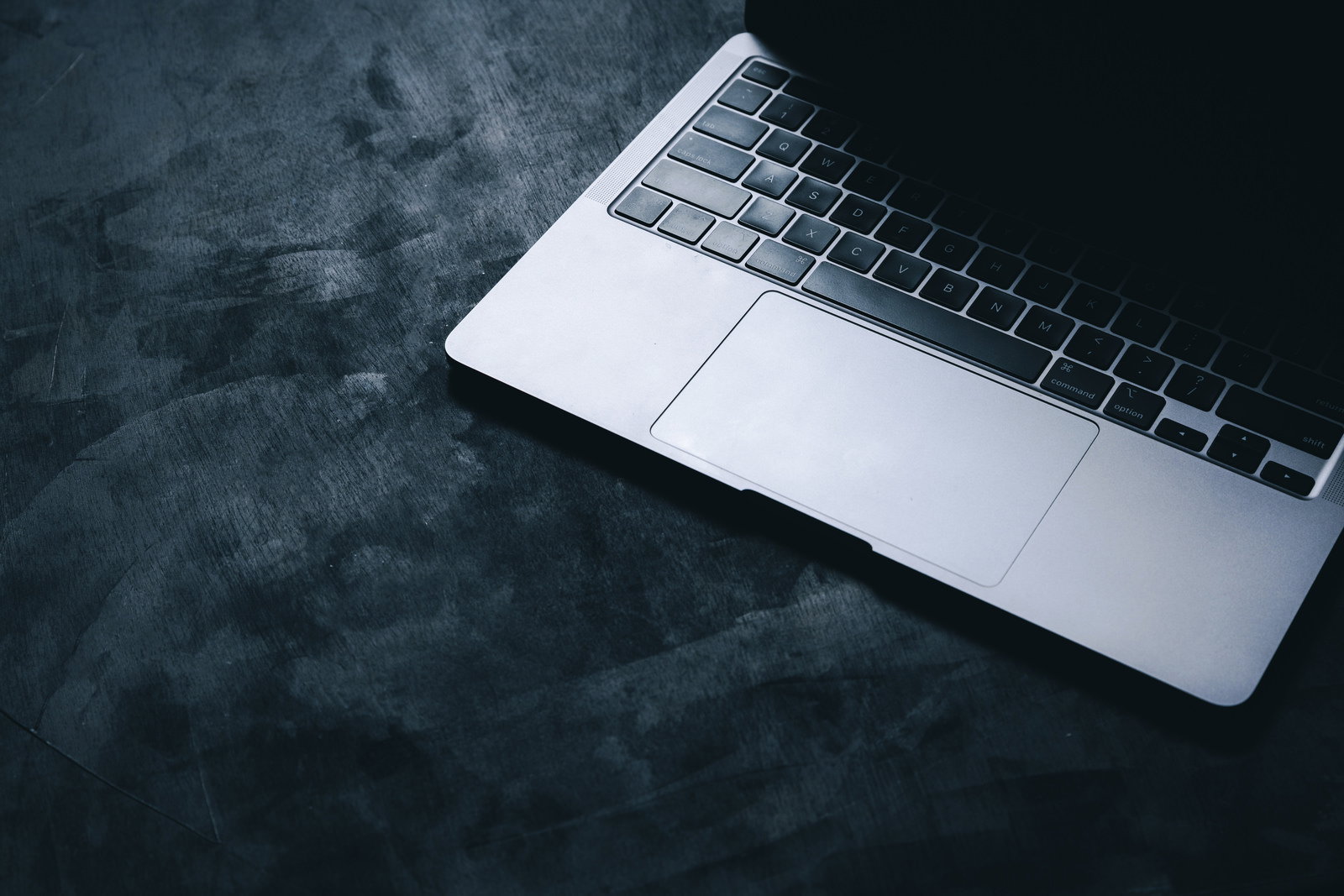 グレーの机の上に置かれた白いノートパソコンの上部が光で照らされている