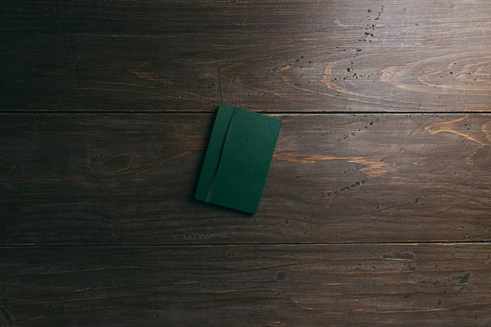 Green notebook placed on wooden floor, overhead view