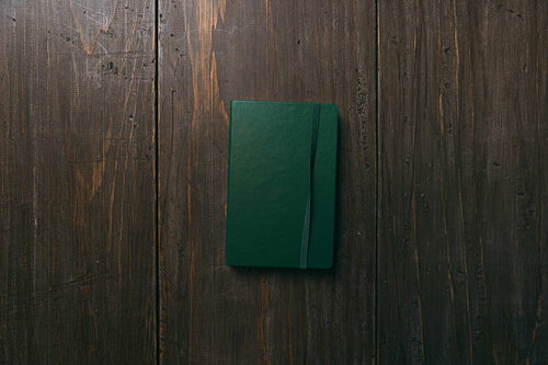古い木目の床に置かれた緑の手帳とペン・筆記用具