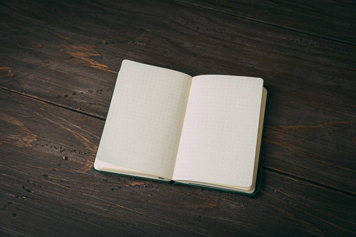 濃い木目のテーブル上に開いたメモ帳と筆記用具