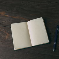 ボールペンと白紙の手帳を木製テーブルに置いた光景の写真