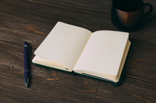 ボールペンで描かれる緑の手帳と白紙、デスクの勉強作業