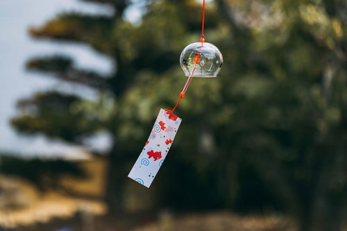 赤い紐の風鈴が風に揺らぐ夏の風物詩、軒下で涼しげに揺れる情景