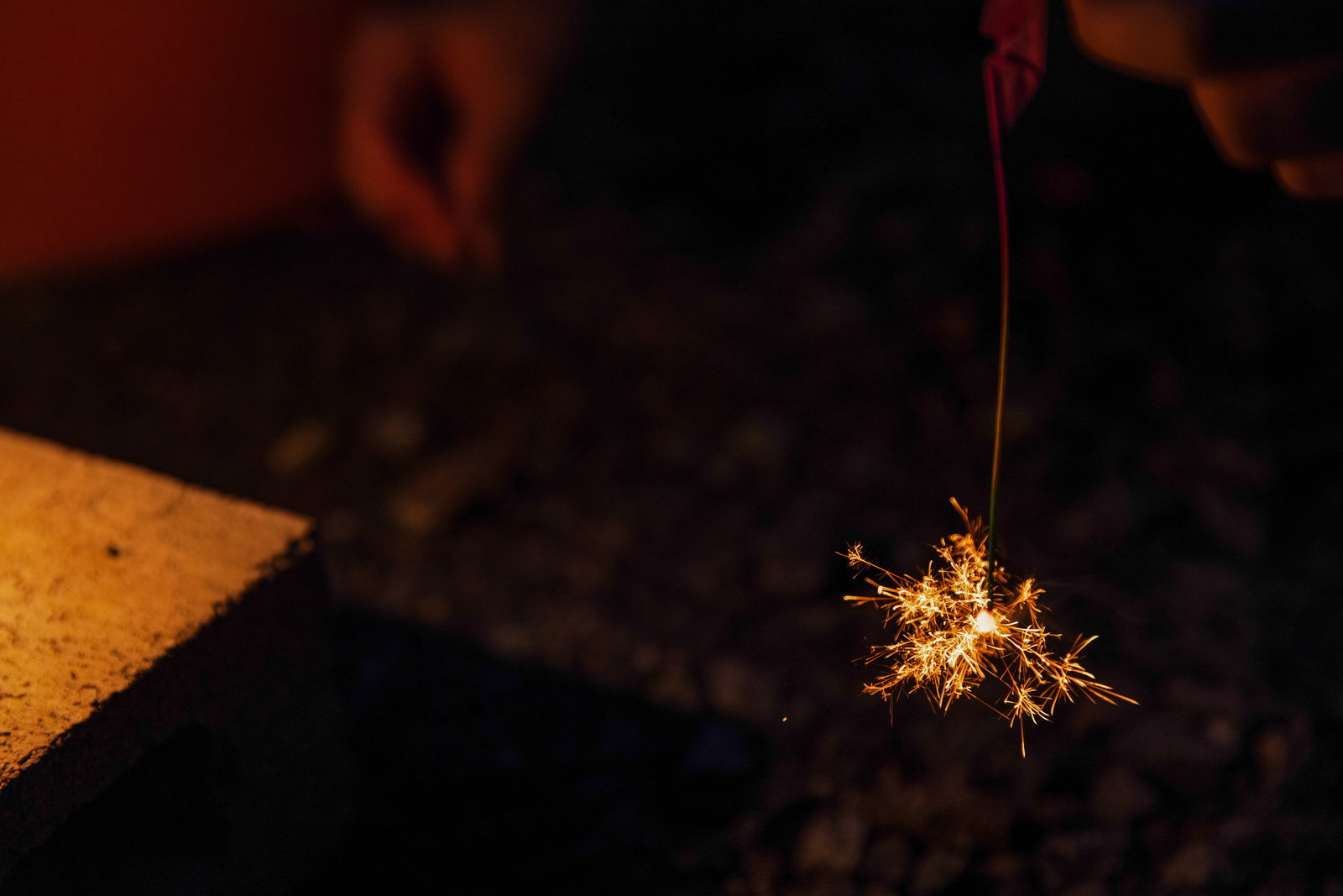 夜間に手から吊るされた線香花火が黄金色の火花を散らしている