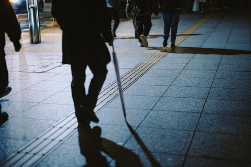 夜間の駅前で傘を持った帰り道、タイル通路を歩く人々