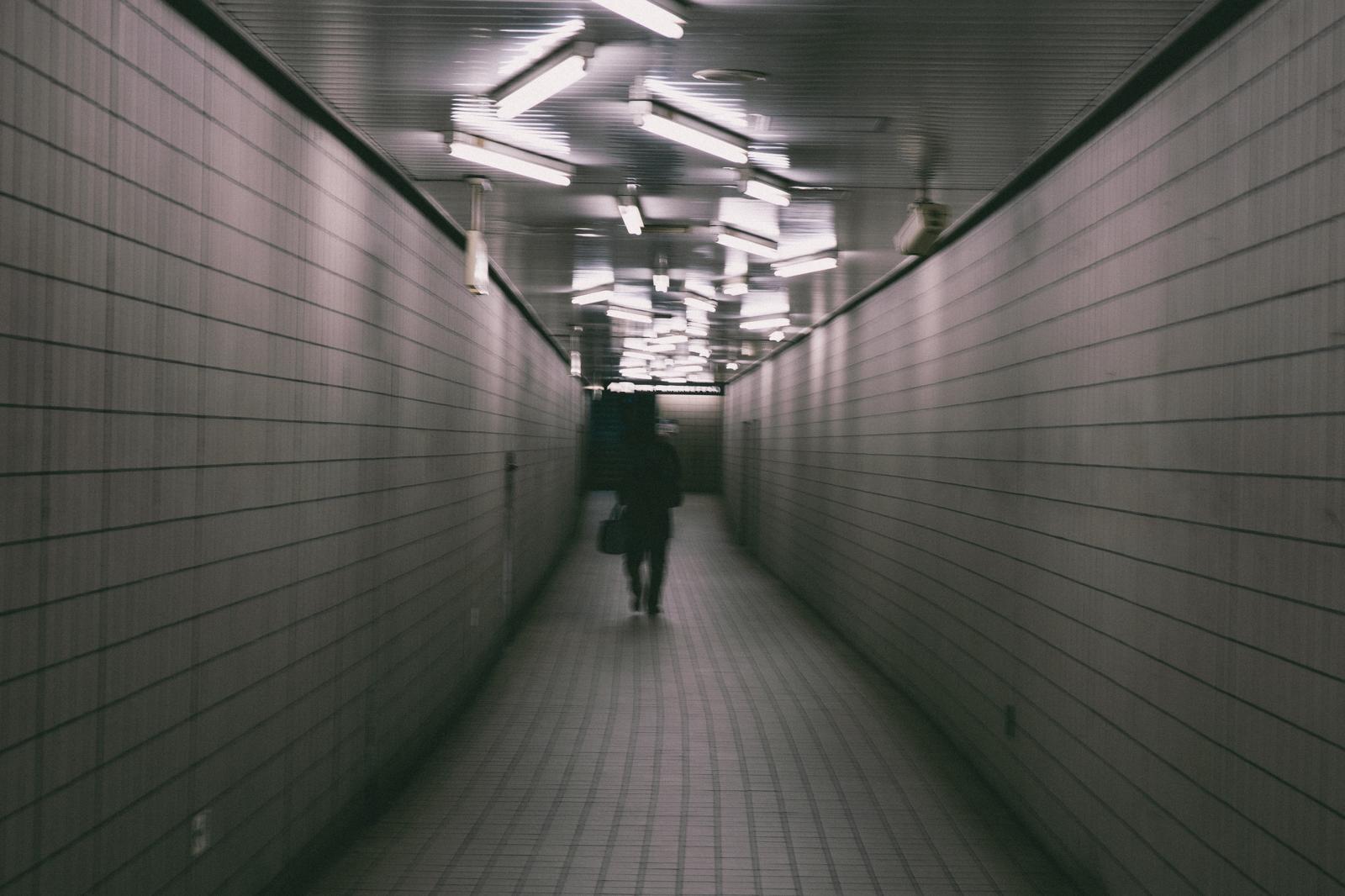 駅の地下通路を進む人物、蛍光灯と白いタイルで構成された直線的な通路